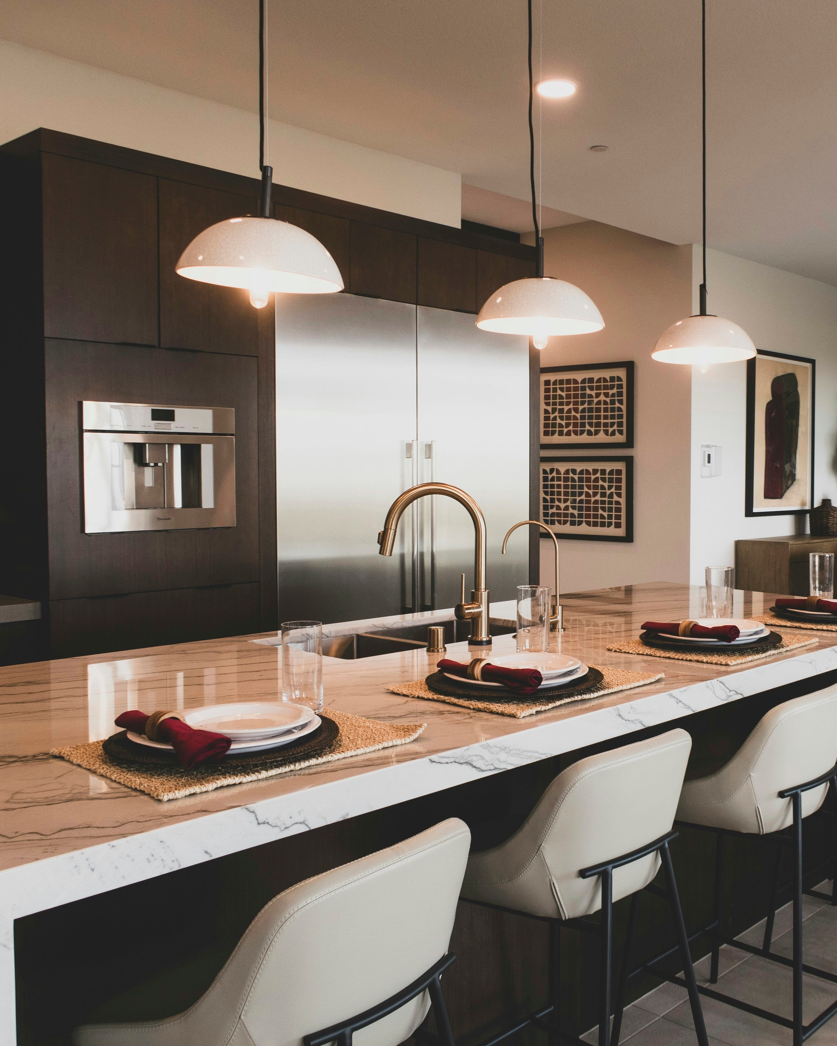 A kitchen with dark wood cabinets, a marble island and pendant lights